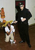 photo: white frat brothers, one in blackface, pose with the student in blackface kneeling on the floor and a student dressed as a cop pointing a prop gun at his head. Ole Miss, Halloween 2001.