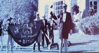 Here is an old black and white photo of several white students in minstrel-show blackface, smiling at the camera and holding a banner reading 'We love the Betas.'