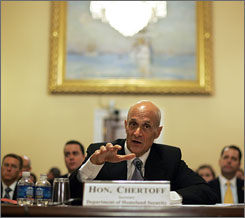 Here is a photo of Michael Chertoff reaching his hand forward while explaining something at a Congressional hearing.